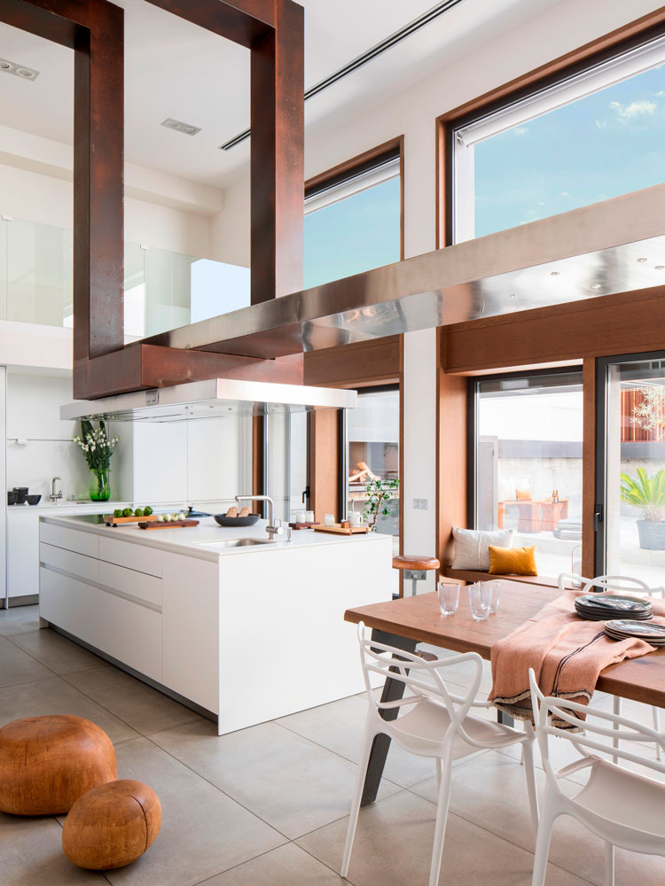 Diseño de interiores de una cocina a doble altura con isla central y una impresionante escultura de hierro fundido y acero.